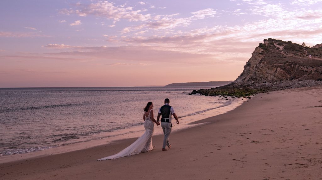 Bride and groom, Carly and Paul, heading into the surest together on a remote beach, Praia da Boca do Rio in Budens, Portugal